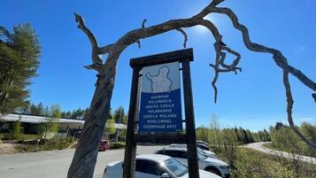 A signboard with multiple names for the Arctic Circle, a parking area with cars, and a clear blue sky.
