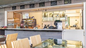Un café con una mesa de vidrio, sillas de madera, una máquina de café y estantes con diversos artículos.