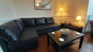 Una sala de estar moderna con un sofá de cuero oscuro, una pequeña mesa de centro con adornos y dos lámparas de noche.