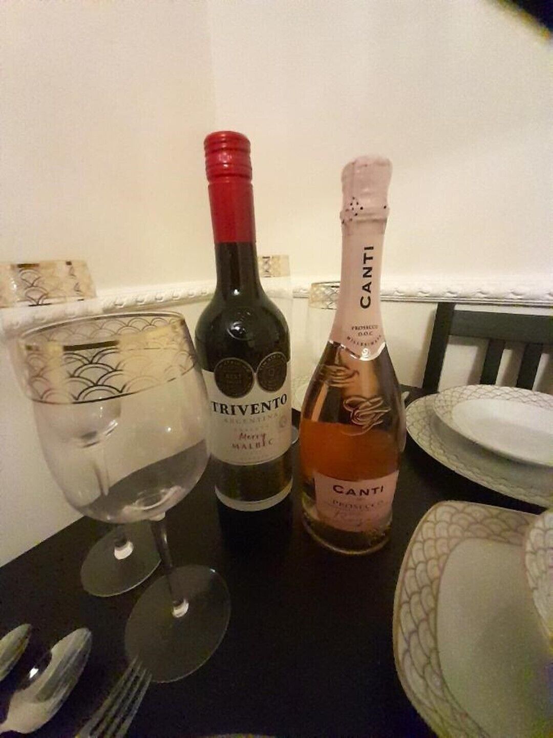 Une table avec deux bouteilles de vin, un verre et des couverts.