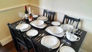 Mesa de comedor lista con platos blancos, cubiertos y vasos, con una botella de vino y un vaso de agua sobre la mesa.