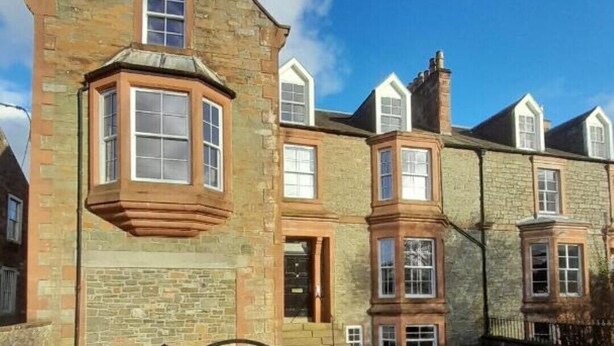 Un edificio histórico de piedra con múltiples ventanas y una placa de piedra que dice 