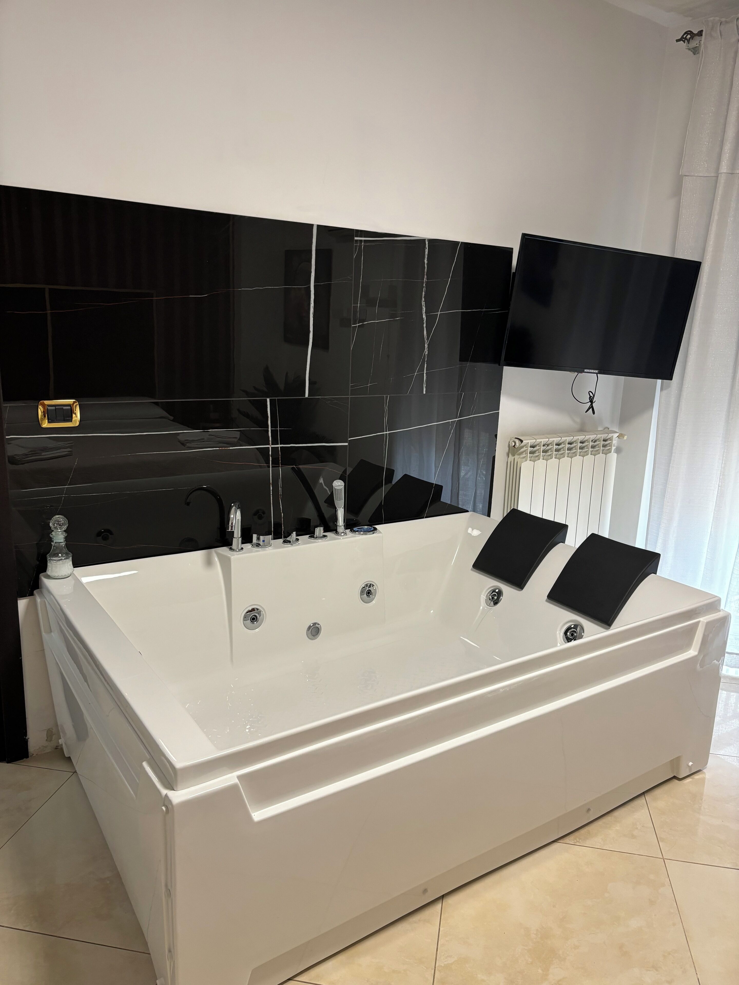 Un baño moderno con una bañera blanca grande, un tocador negro, un televisor de pantalla plana montado sobre el tocador y un radiador en la pared.