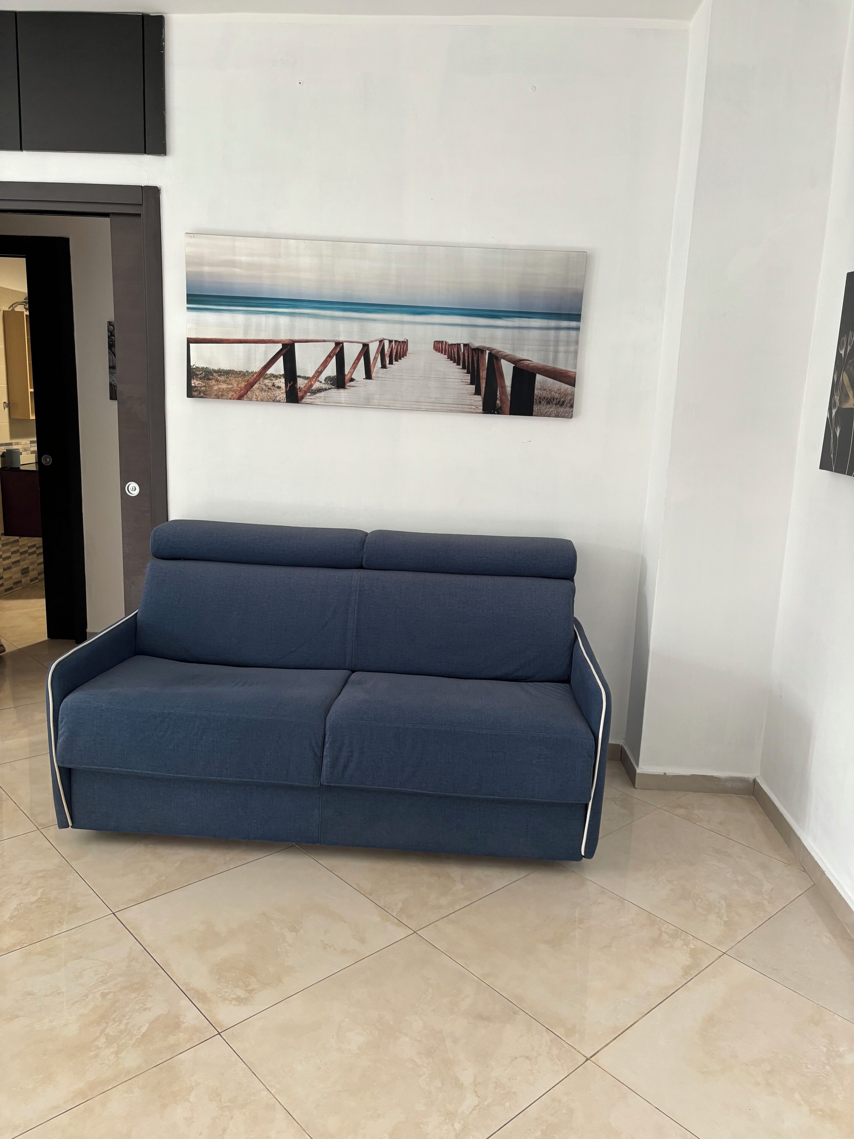 Una sala de estar moderna con un sofá azul, un cuadro abstracto grande y un suelo de baldosas.