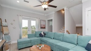 Ein modernes Wohnzimmer mit einem petrolfarbenen Ecksofa, einem Holztisch und einem Deckenventilator.