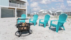 Ein Anwesen am Strand mit einem zweigeschossigen Gebäude, einer Sitzgelegenheit im Freien mit türkisfarbenen Stühlen und einer Feuerstelle.