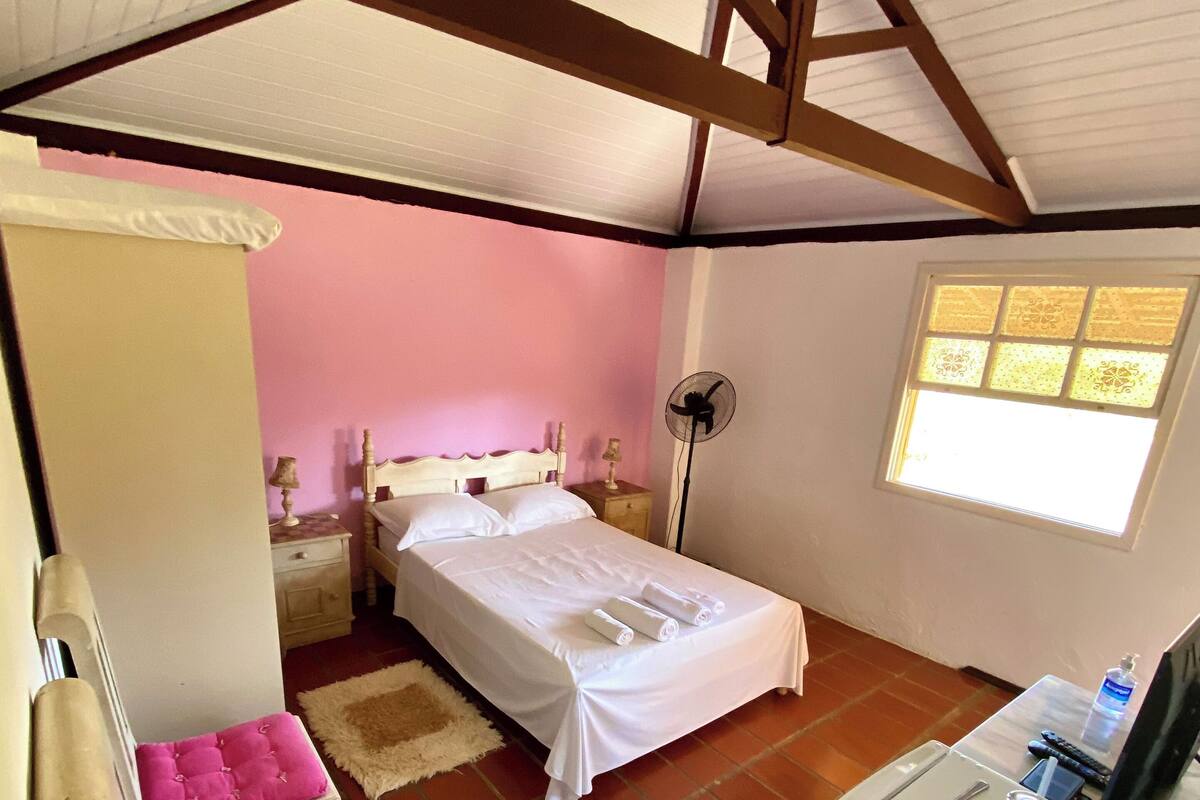 Ein Schlafzimmer mit Bett, Stuhl, Schreibtisch, Ventilator und Fenster.