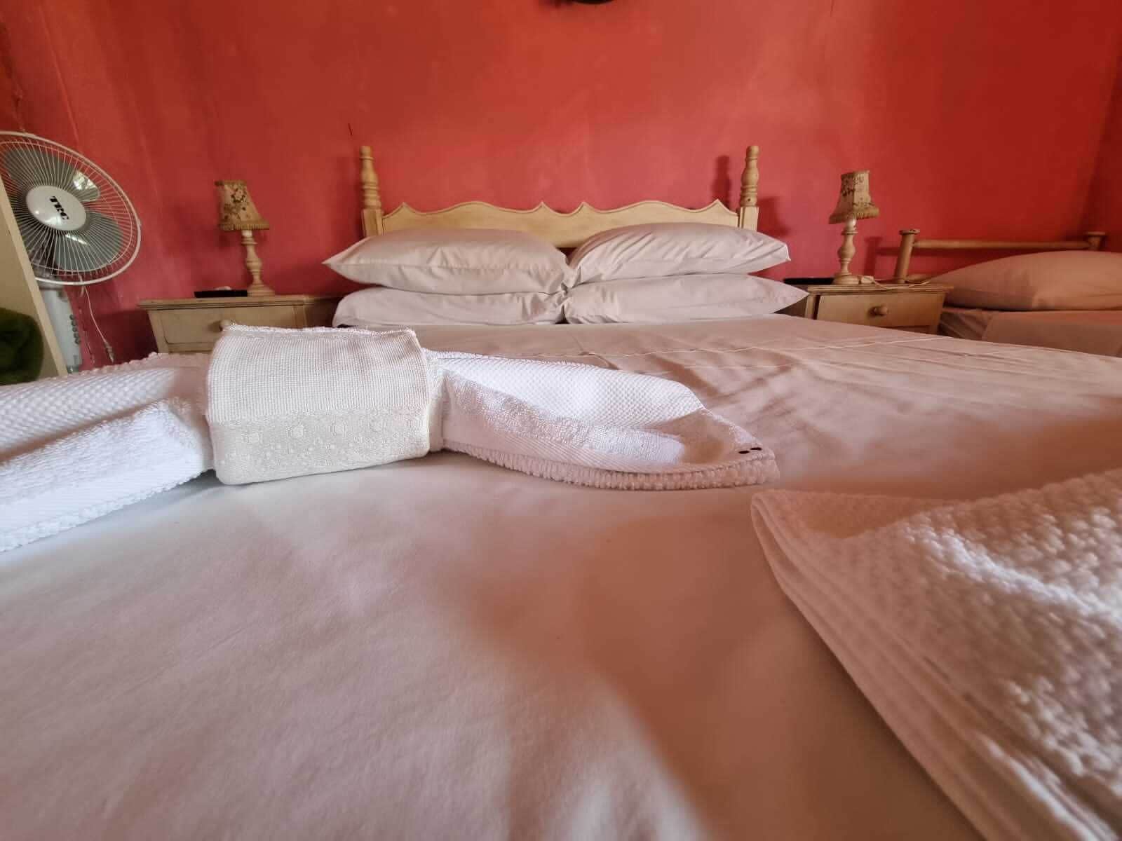A neatly made bed with white linens and pillows, a wooden headboard, and a bedside table with a lamp.