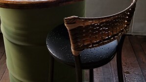 A round table with a wooden top and a green cylindrical base, accompanied by a wicker chair with a black seat. - Villa Bella do Turvo Pousada Gastrobar (Andrelandia)