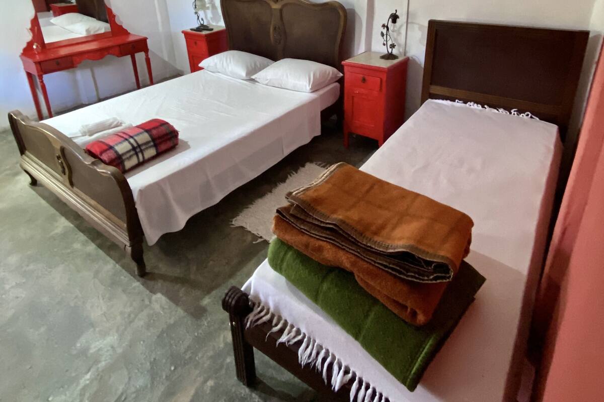 Ein Schlafzimmer mit zwei Einzelbetten, einem Holzstuhl, einem kleinen Tisch und drei an der Wand befestigten Bilderrahmen.