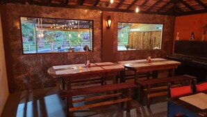 A restaurant with wooden tables and benches, large windows with views of greenery, and a bamboo screen. - Villa Bella do Turvo Pousada Gastrobar (Andrelandia)