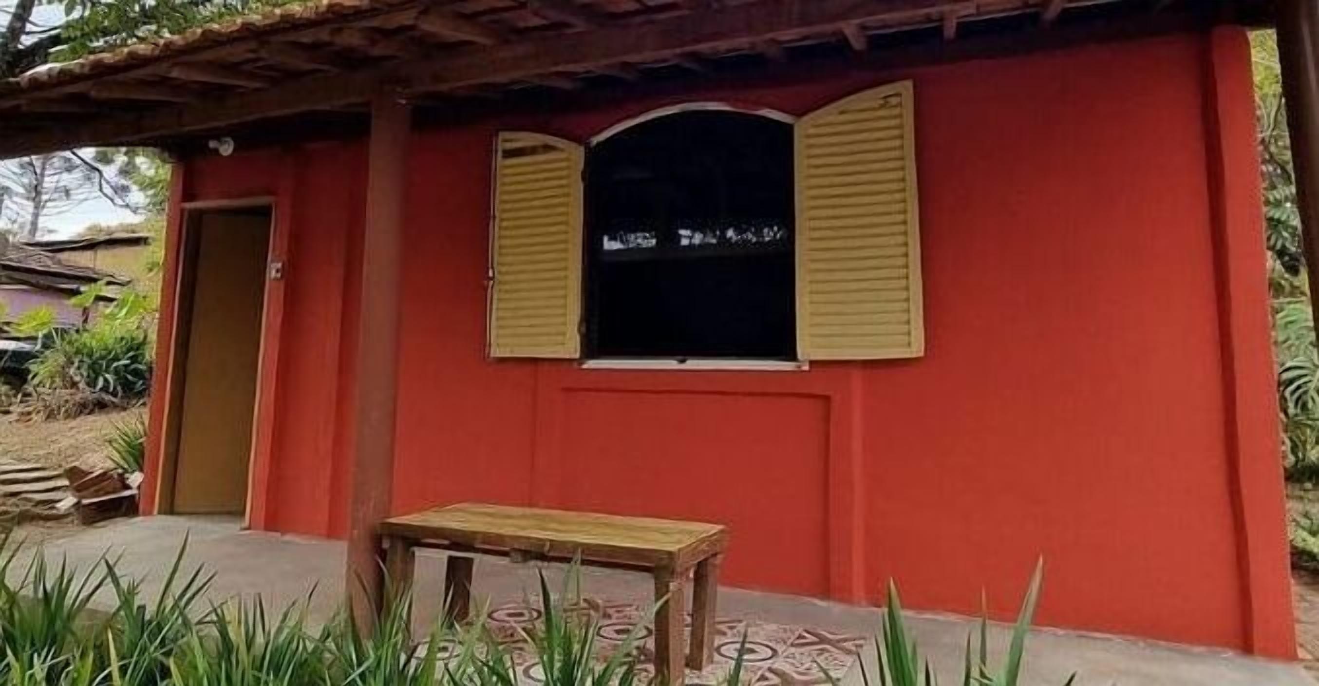 A red building with two windows, a door, and a small table in front.