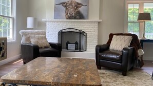 Een woonkamer met een open haard, twee leren fauteuils, een salontafel en een groot schilderij boven de haard.