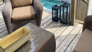 Een terras met een rieten stoel, een glazen tafel en een hottub.