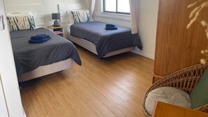 A bedroom with two beds, a window with curtains, a bedside table with a lamp, and a wicker chair. - Apartment Ricardo - 200m to the beach (Armação de Pêra)