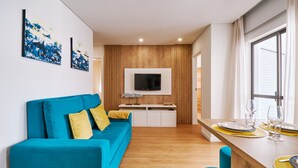 A modern living room with a blue sofa, wooden panel wall, and a TV mounted above a white cabinet. - Apartment Ricardo - 200m to the beach (Armação de Pêra)