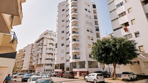 A multi-story residential building with balconies, parked cars, and a tree in front. - Apartment Ricardo - 200m to the beach (Armação de Pêra)