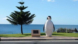 A penguin statue next to a tree and a bench by the ocean. - Cozy Unit in Penguin (Penguin)