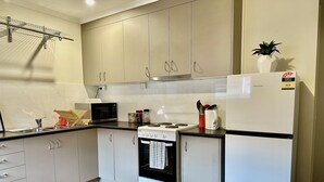A modern kitchen with grey cabinets, a microwave, stove, and a refrigerator. - Cozy Unit in Penguin (Penguin)