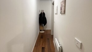 A narrow hallway with wooden flooring, white walls, a ceiling light, and a coat rack with jackets. - Cozy Unit in Penguin (Penguin)