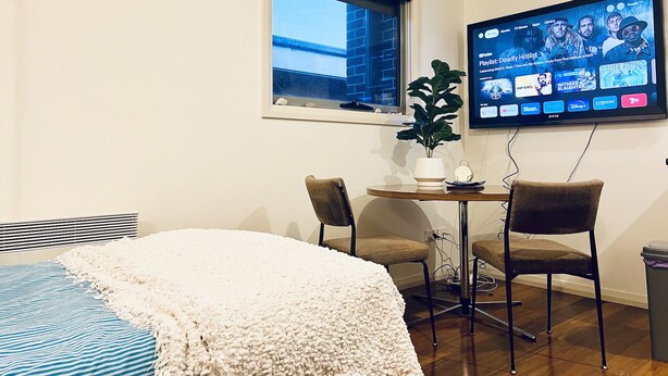 A hotel room with a bed, a desk with a computer, a window, and a TV displaying a movie list. - Cozy Unit in Penguin (Penguin)