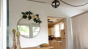 Une console en bois, agrémentée d’un miroir et de bougies, un tapis à motifs et une cuisine visible à travers une porte ouverte.