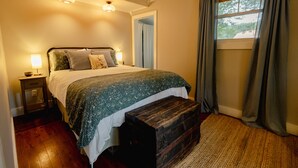 Une chambre à coucher avec un lit, des lampes de chevet, un banc en bois, une fenêtre avec des rideaux et une porte.