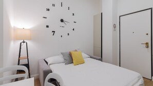 Een kamer met een bed, een wandklok, een lamp, een deur en een stoel.