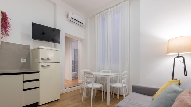 Een knus woongedeelte met kitchenette, een eethoek met stoelen, een bank en een lamp.