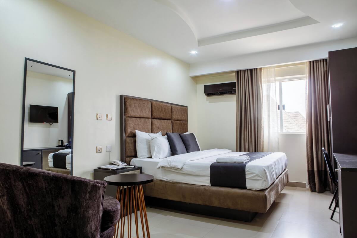 A modern hotel room with a large bed, a flat-screen TV, a desk, and a chair.