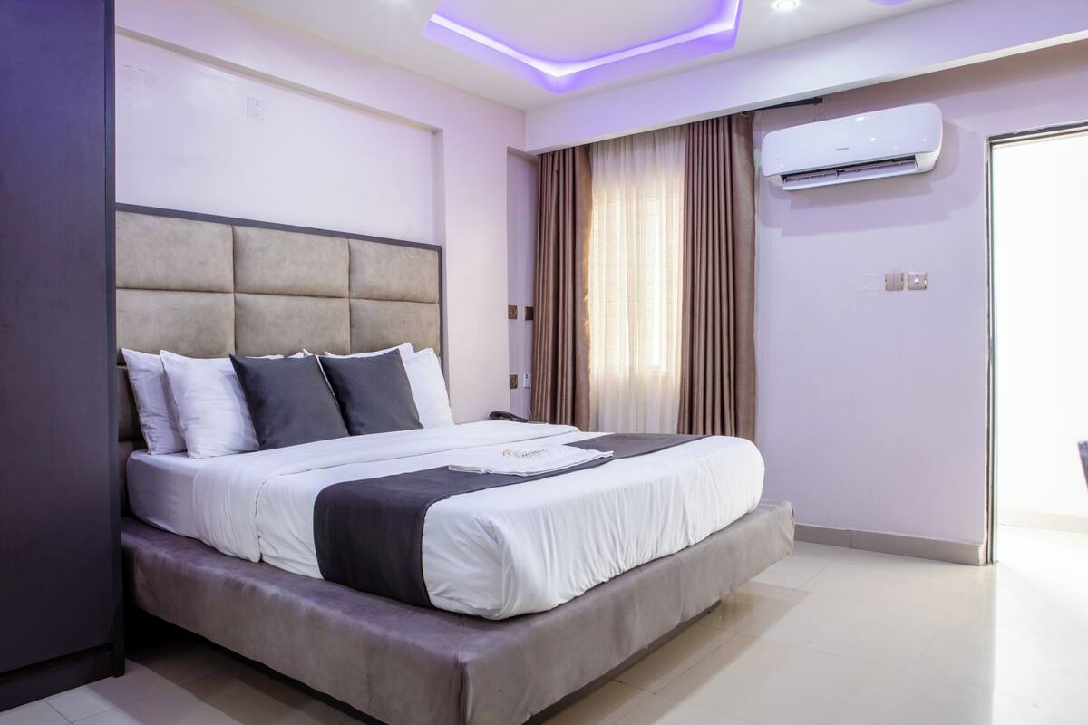 A modern hotel room with a large bed, air conditioning unit, and a view of the outside.