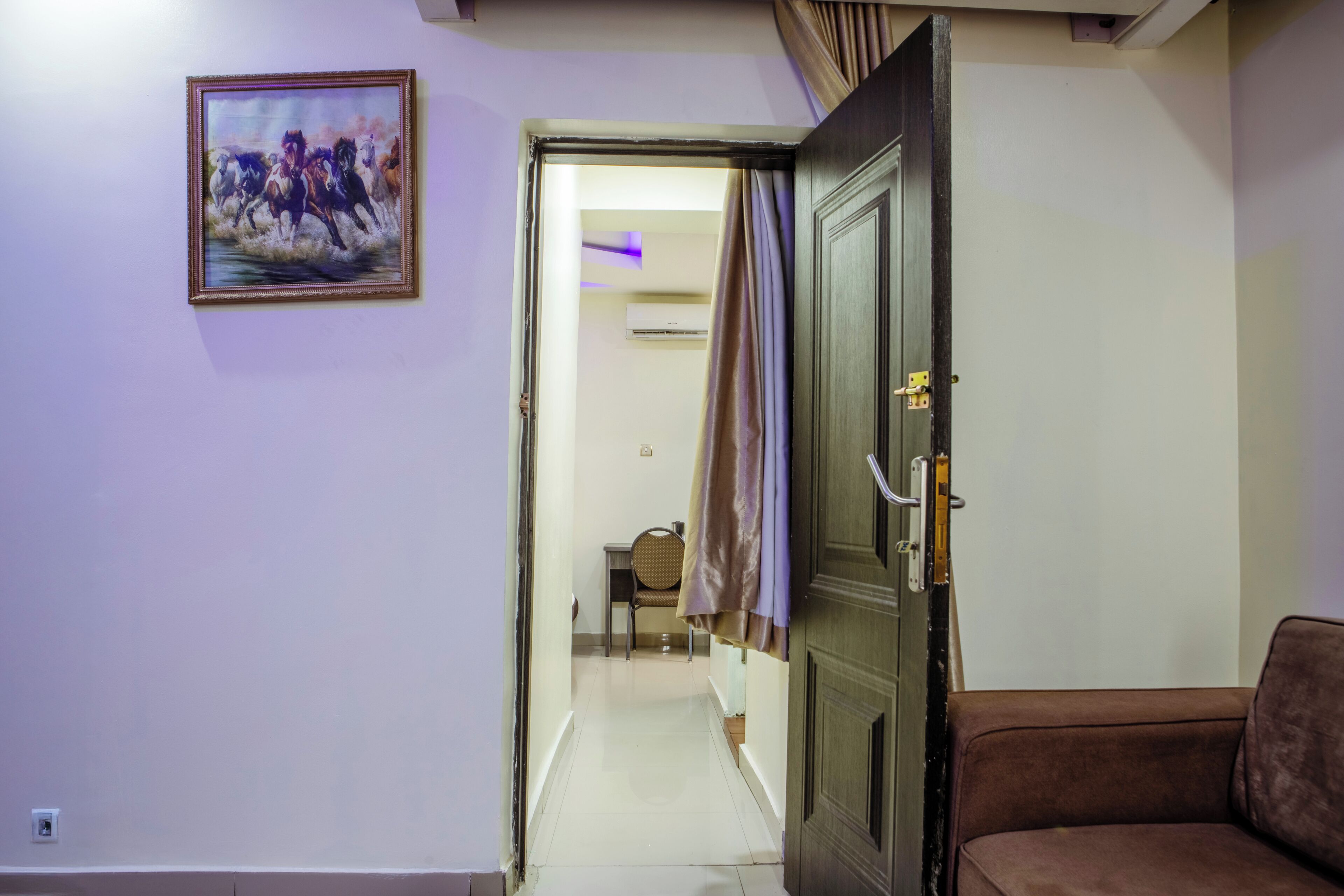 A hallway with a door, a framed painting, a chair, and a sofa.