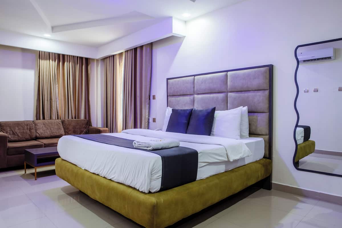 A modern hotel room with a large bed, a sofa, and a mirror.