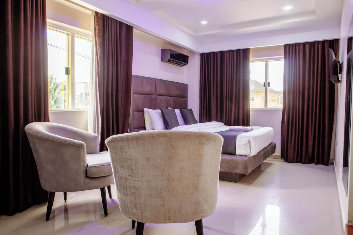 A hotel room with a bed, two armchairs, a large window, and an air conditioning unit.