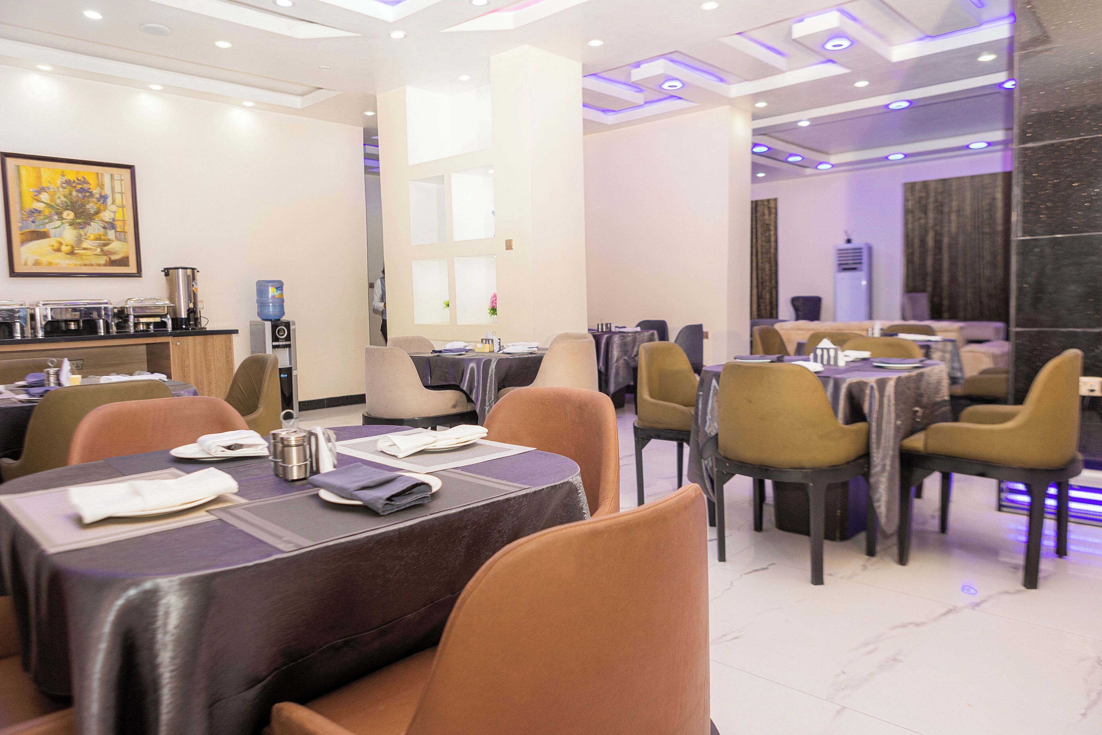 A hotel dining area with multiple tables and chairs, a water dispenser, and a coffee machine.