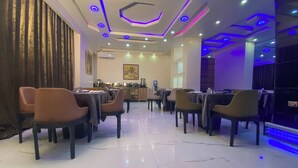 A modern dining area with tables and chairs, a kitchen in the background, and a ceiling with geometric lighting. - Hotel Romeneo (Lagos)