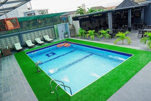 A swimming pool with artificial grass, lounge chairs, and a covered outdoor seating area. - Hotel Romeneo (Lagos)