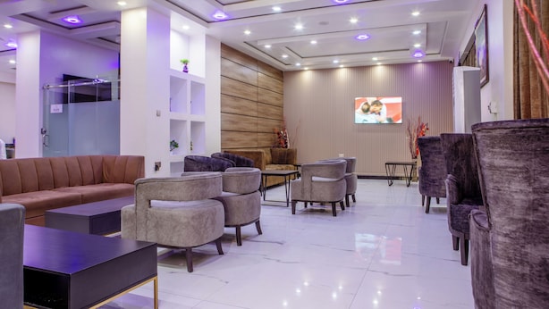 A modern hotel lobby with a sofa, armchairs, a coffee table, a TV, and a wooden accent wall.