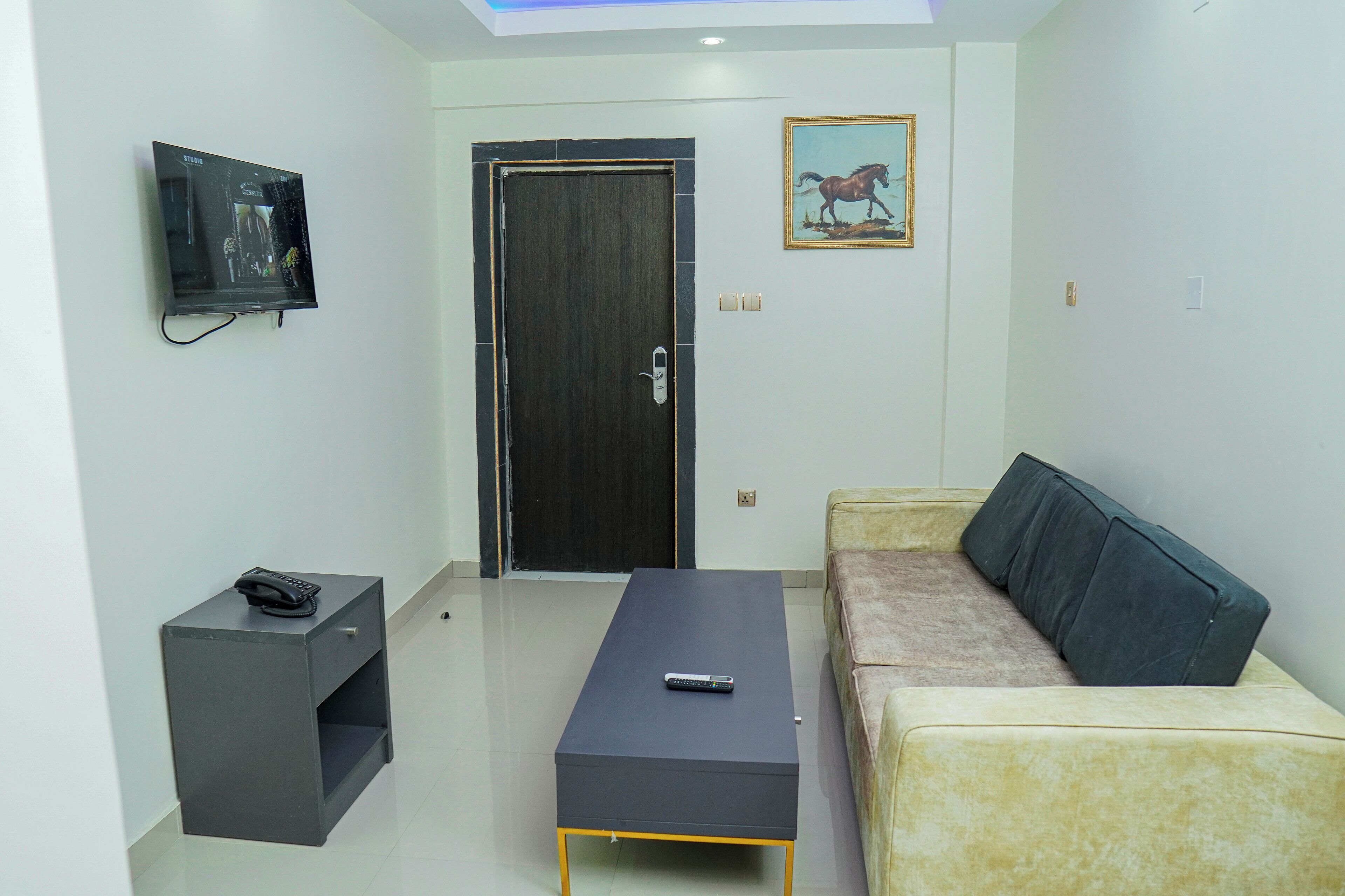 A living room with a sofa, a coffee table, a TV mounted on the wall, and a door.