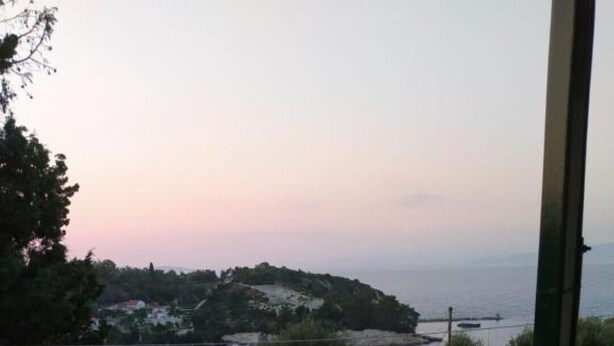 Un balcone con vista sul paesaggio costiero, che include una spiaggia e una zona collinare con edifici.