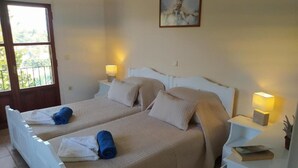 Un letto matrimoniale con biancheria beige e due cuscini, un comodino con una lampada, e una finestra vista sul verde.
