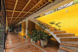 A covered outdoor corridor with a yellow wall, a staircase, and potted plants. - A spacious, 2 bed Penthouse with private pool & parking in Manuel Antonio. (Quepos)
