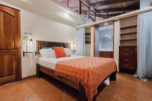 A bedroom with a bed, a nightstand, a wooden wardrobe, and a bathroom visible through an open door. - A spacious, 2 bed Penthouse with private pool & parking in Manuel Antonio. (Quepos)