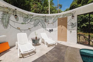 A sunlit outdoor area with white lounge chairs, a small table, and a decorative wall mural. - A spacious, 2 bed Penthouse with private pool & parking in Manuel Antonio. (Quepos)
