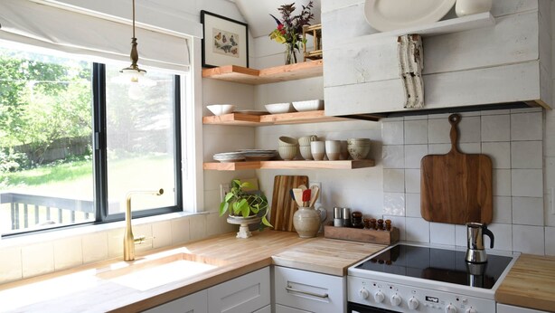 A kitchen with a wooden countertop, white cabinets, a stove, and a window with a view of greenery.