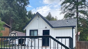 A small, single-story house with a white exterior and dark roof. It features a front porch with a black railing and a staircase leading up to the entrance.