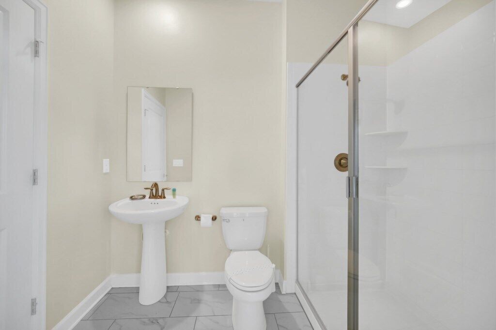 A bathroom with a pedestal sink, toilet, and a glass shower enclosure.