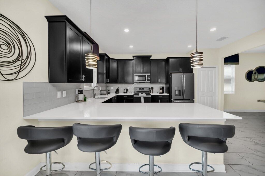 A modern kitchen with dark cabinetry, a white island, and three black bar stools.