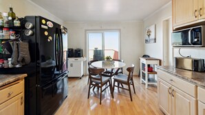 A modern kitchen with a black refrigerator, wooden cabinets, a dining table with chairs, and a view through a large window. - SF Home with SPECTACULAR VIEW- Minutes to downtown (San Francisco)
