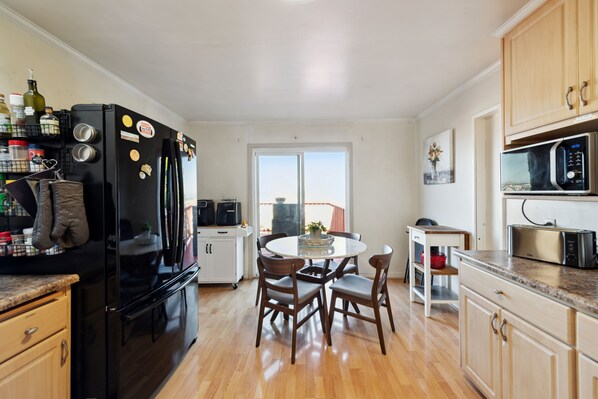A modern kitchen with a black refrigerator, wooden cabinets, a dining table with chairs, and a view through a large window. - SF Home with SPECTACULAR VIEW- Minutes to downtown (San Francisco)